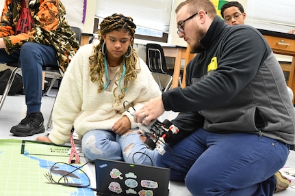 IMAGE: Naval Surface Warfare Center Dahlgren Division computer scientist Jonathan Clark helped eighth grade students at Walker-Grant Middle School problem solve one of the most difficult activities, which was programming the robot to move forward, pick up a box and then return to where it started.
