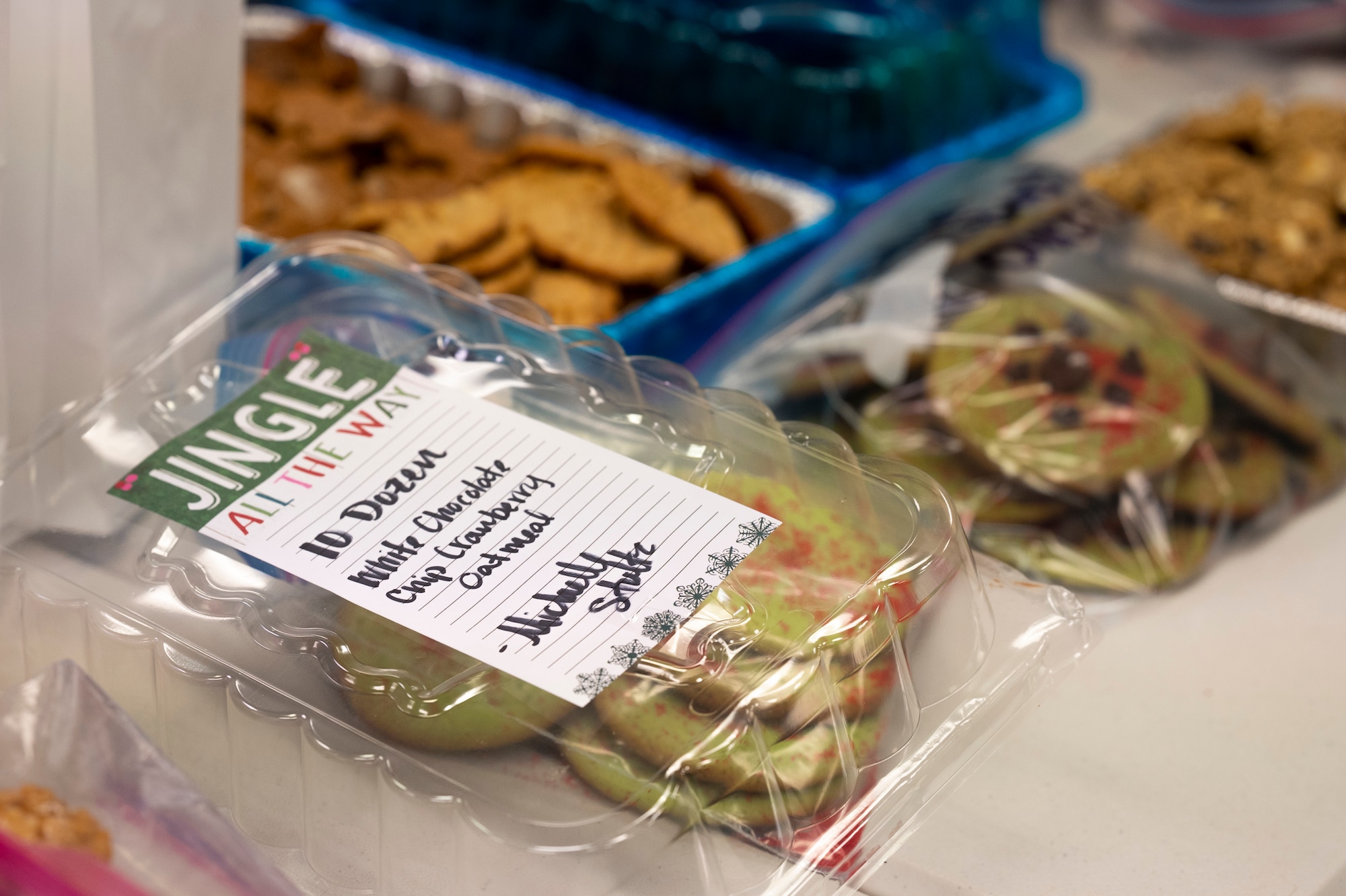 Batches of cookies are laid on a table; one tray has a sticky note from a donor.