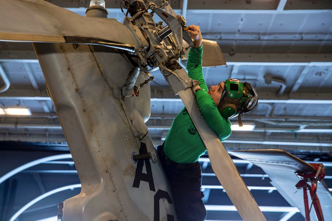 A sailor works on the propeller of a helicopter aboard a ship at sea.