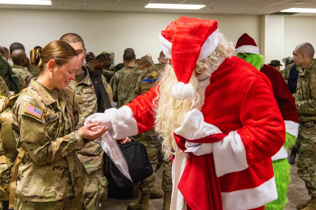 Santa Claus puts a gift in a soldier’s hand as a group of soldiers gather in the background.