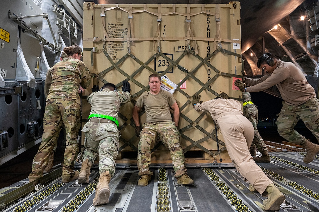 Airmen push cargo off an aircraft.