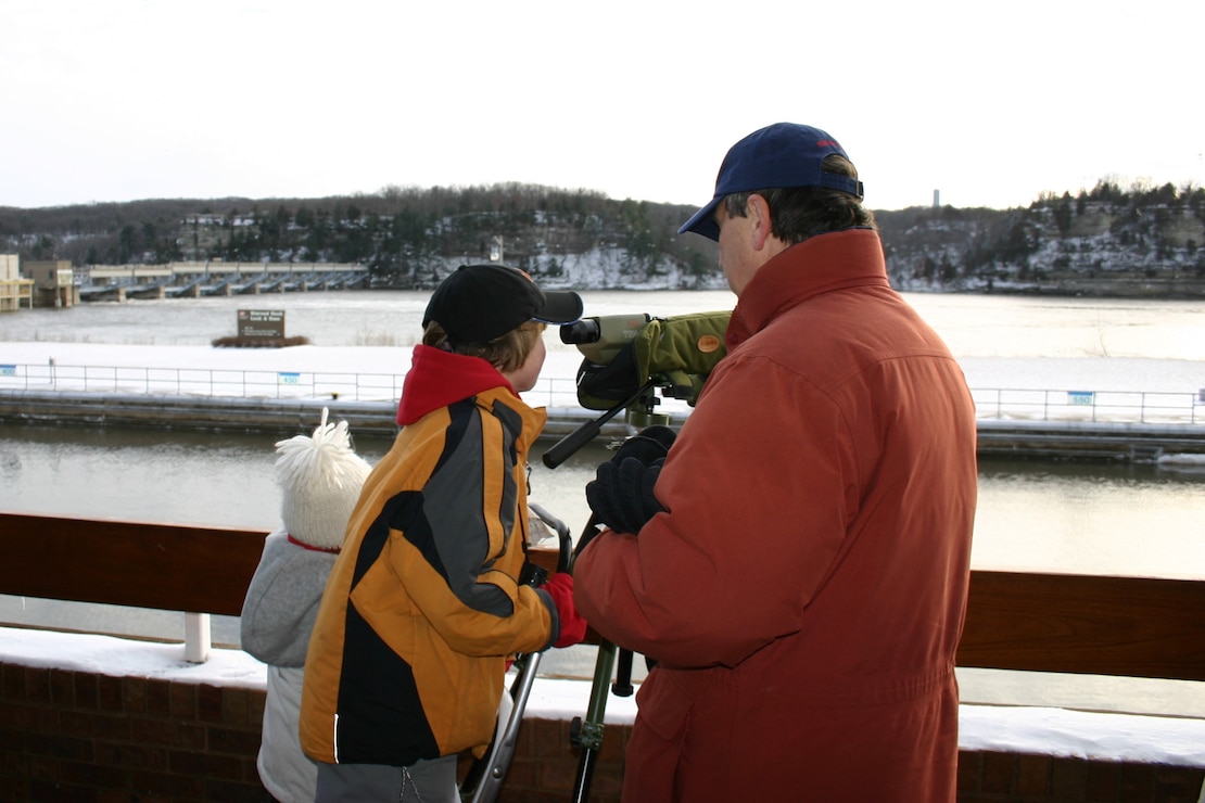 A volunteer assists a child with viewing eagles through a spotting scope on the deck of the Illinois Waterway Visitor Center.
