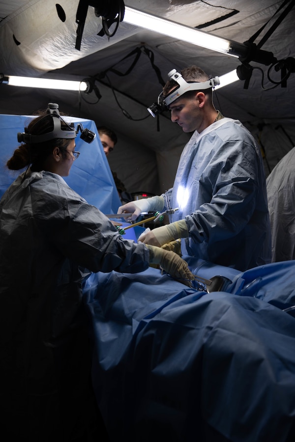 U.S. Navy Lt. Bash Sarkar, a general surgeon, left, and Lt. Josh Cotler, an orthopedic surgeon, both with 3rd Medical Battalion, simulate a medical operation during a field medical training exercise at Kin Blue Training Area, Okinawa, Japan, Dec. 11, 2022. 3rd Med. Bn. regularly conducts Role II medical facility training and assessments in a field environment in order to rehearse providing care in a combat scenario. (U.S. Marine Corps photo by Lance Cpl. Sebastian Riveraaponte)