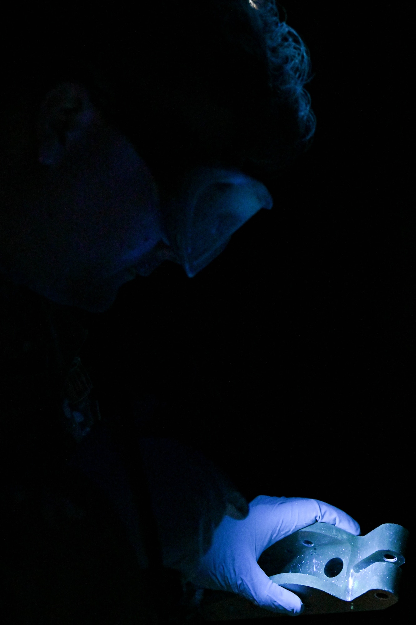 U.S. Air Force Tech. Sgt. Cody Dickerson, 23rd Maintenance Squadron nondestructive inspection supervisor, looks at a cracked piece of metal under ultraviolet-light during an inspection at Moody Air Force Base, Georgia, Dec. 5, 2022. This technique detects cracks inside aircraft parts to prevent risks to flight safety. (U.S. Air Force photo by Senior Airman Rebeckah Medeiros)