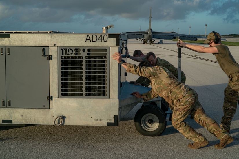 A photo of Airmen pushing a power cart on the flightline.