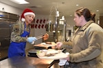 U.S. Air National Guard Airman 1st Class Dewaun Blair, 185th Air Refueling Wing Food Services, serves prime rib to Airmen while wearing a Santa hat during the December training weekend at the 185th Air Refueling Wing in Sioux City, Iowa, Dec. 3, 2022. Services prepares special holiday meals for Airmen during the holiday season typically with orders made through the Defense Logistics Agency's Subsistence supply chain. DLA Troop Support, located in Philadelphia, PA,  is a Major Subordinate Command of the Defense Logistics Agency, with a global presence including offices in Europe & Africa and the Pacific regions. (U.S. Air National Guard photo by Senior Airman Tylon Chapman)