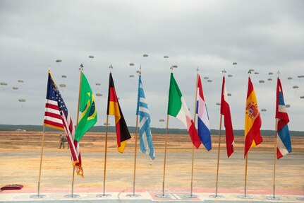 The flags of allied partner are proudly displayed on Sicily Drop Zone, Fort Bragg, NC, as paratroopers from the U.S. Civil Affairs Command (Airborne) alongside local Fort Bragg and partner nations' airborne Soldiers, gently drift from the sky during the the Randy Older Memorial Operation Toy drop 2.0, a combined airborne training event held from 4-12 DEC 2022 to increase joint airborne proficiency and enhance community relations.