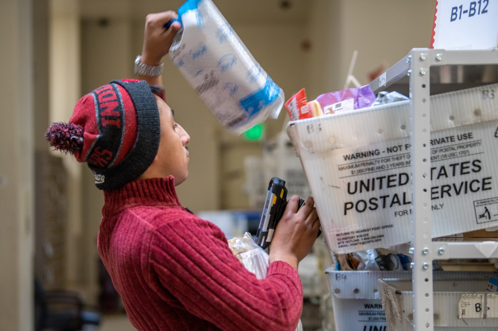 A postal clerk pulls a package from a mail bin