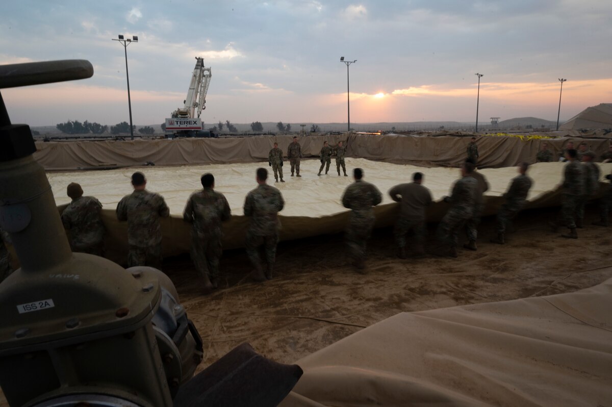 386th Air Expeditionary Wing Airmen unroll a fuel bladder during an installation at Ali Al Salem Air Base, Kuwait, Dec. 22, 2022. Working in unison together, the team cut down the installation time to just ten minutes. (U.S. Air Force photo by Staff Sgt. Dalton Williams)