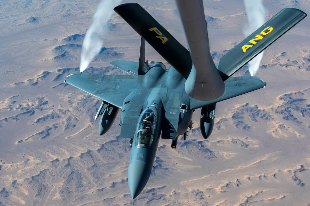 An aircraft releases smoke from its wings while receiving fuel via the boom from another aircraft.