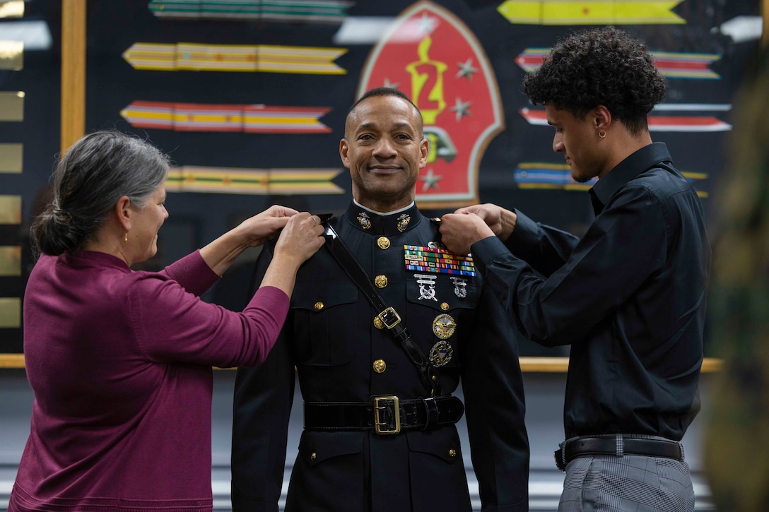 A woman and a young man place pins on the uniform of a Marine standing between them.