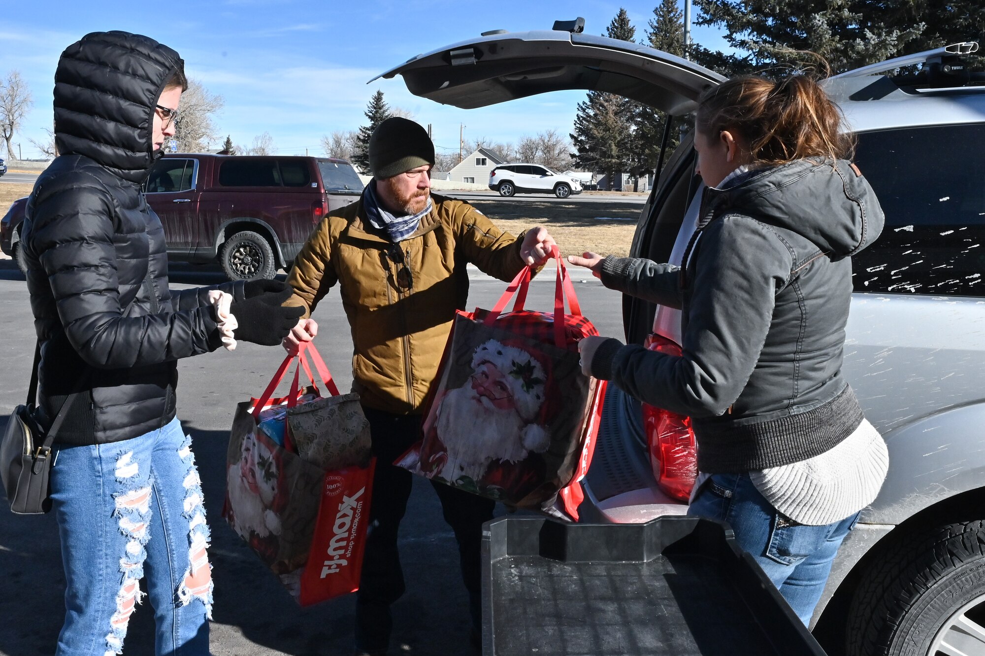 David Cook, 90th Contracting Squadron contracting specialist, hands presents to Sara Cook, 90 CONS agency/organization program coordinator, and Senior Airman Kyra Blystone, 90 CONS contracting officer, to drop them off for local families in need as part of Needs Inc Adopt a Family Program in Cheyenne, Wyoming, Dec 19, 2022. 90 CONS came together for the second year in a row to support two families in need, so they did not have to choose between giving their kids food or celebrating the holiday season. (U.S. Air Force photo by Joseph Coslett Jr.)
