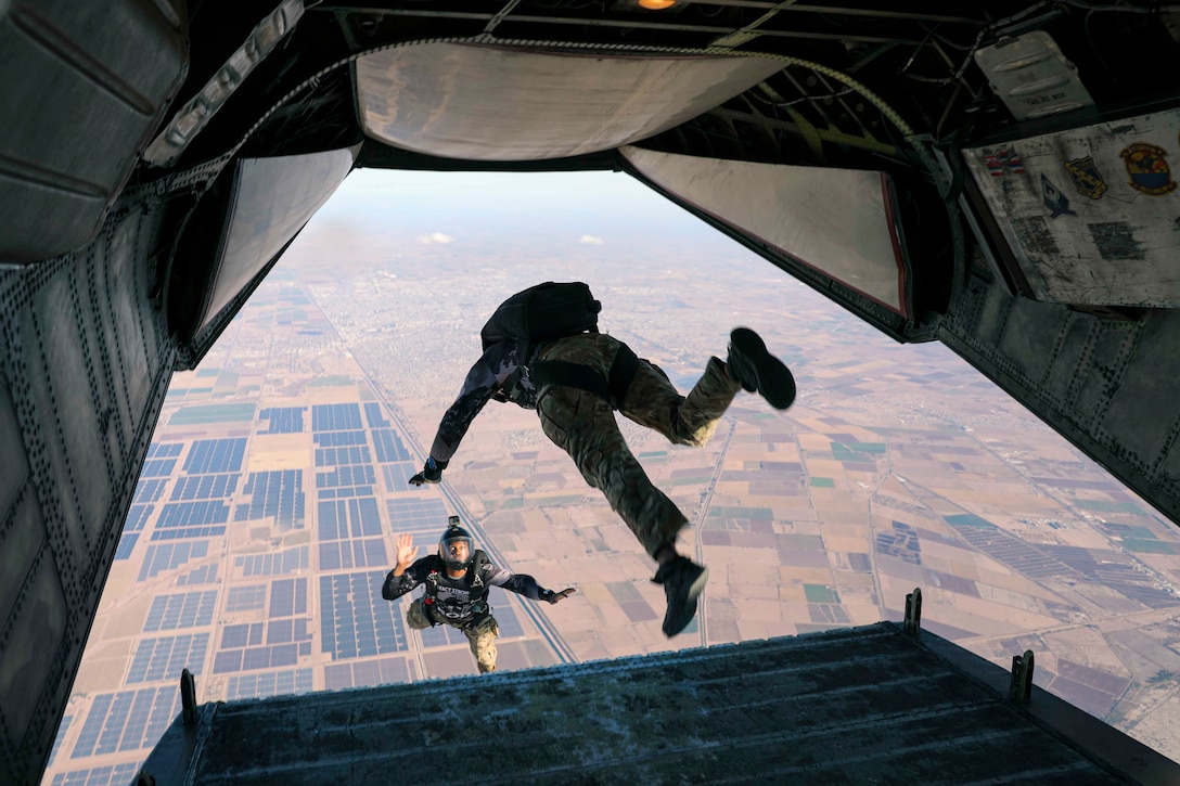 Two sailors jump out the back of an airborne aircraft.