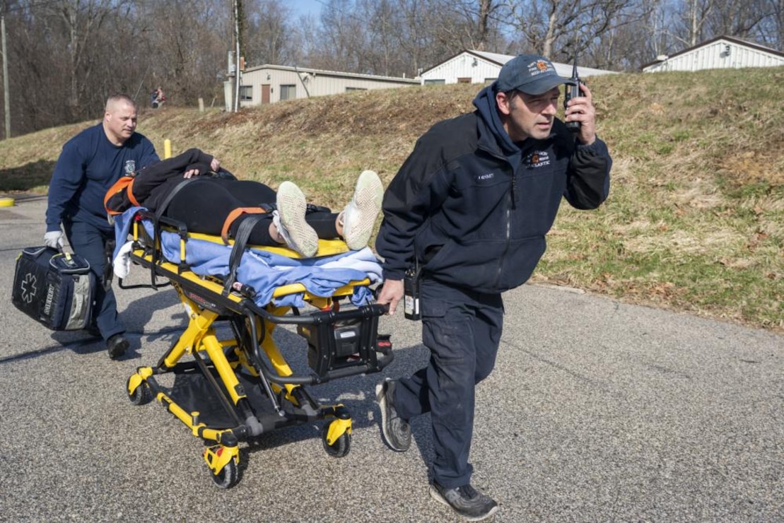 Naval Support Actiivty Crane Firefighter Paramedic Justin Disney (right) and Firefighter Emergency Medical Technician Mickael Harris (left) cart a mock victim to an ambulance during an installation exercise on March 15, 2022. Installation police, fire, paramedics, and explosive ordnance disposal participated in the exercise, which culminated in simulating an aerial evacuation with local-area partners. (Official U.S. Navy photo by Jeff M. Nagan)