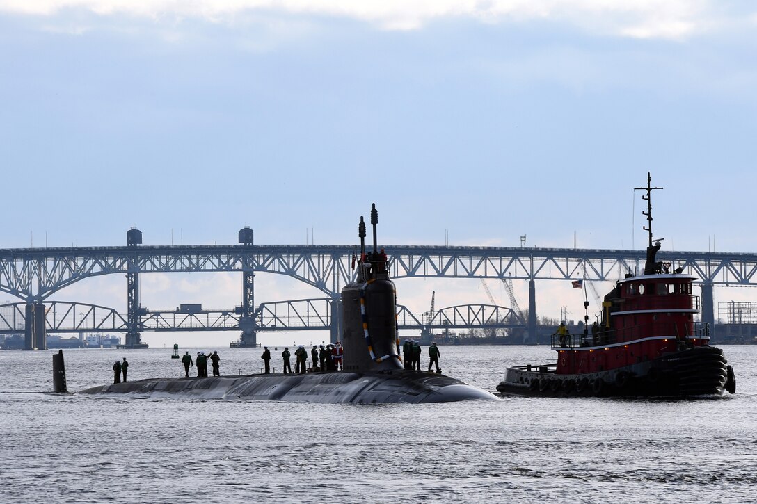 A submarine is shown in the water with military members standing atop.