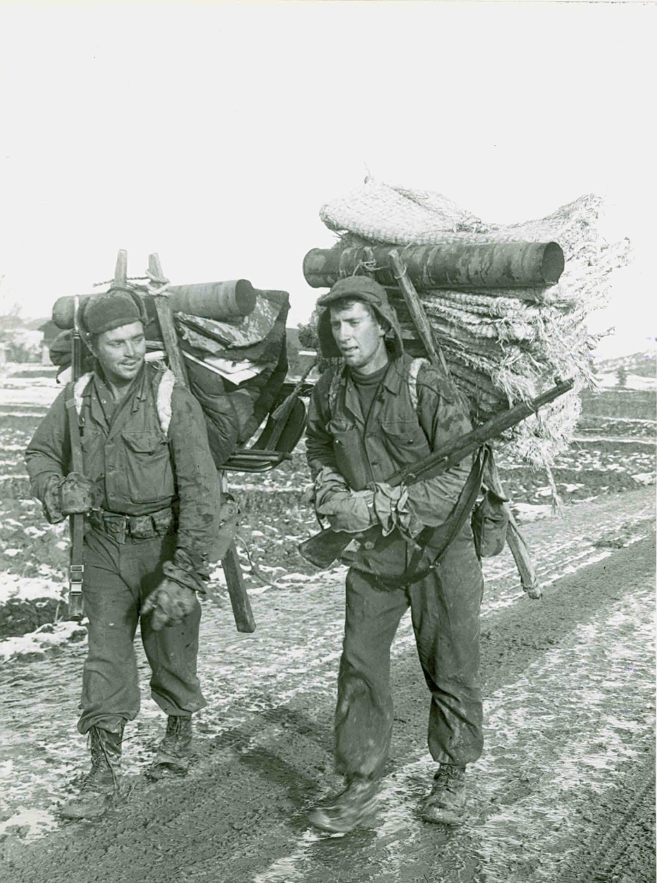 Two men walk along a slush-covered road with giant packs on their backs.