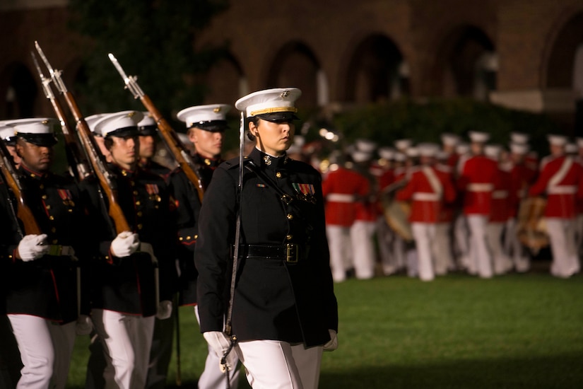 A woman carrying a sword over her shoulder marches ahead of men who follow.