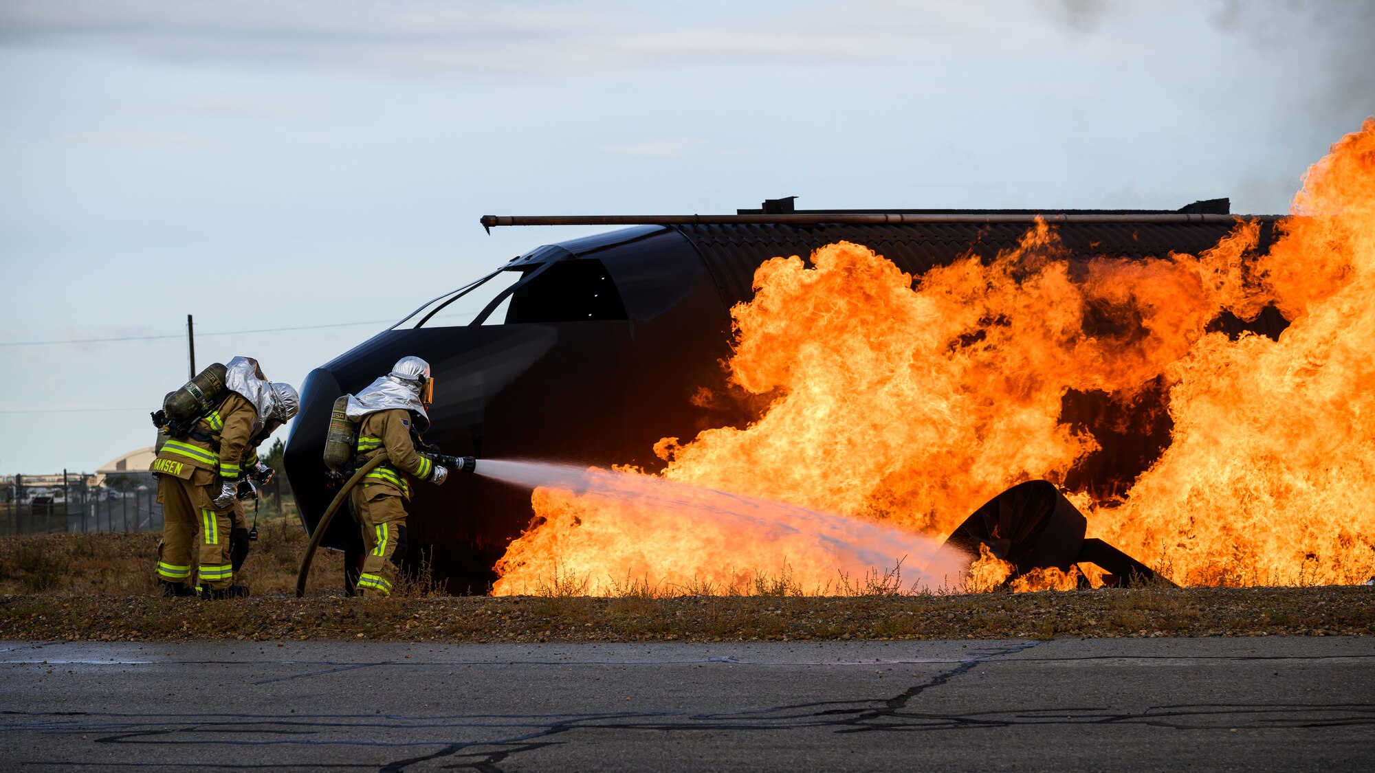 two firefighters pour water on flames.