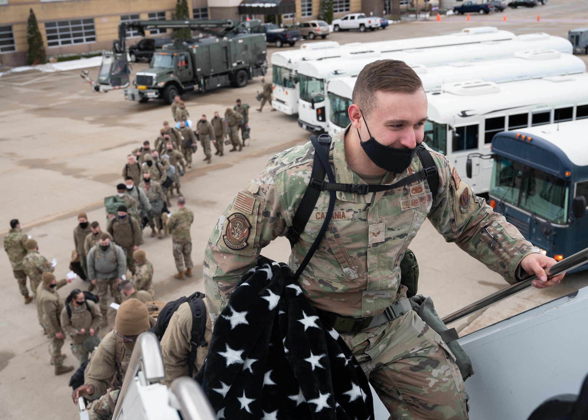 Military men and women walk up rolling stairs into a transport plane