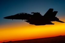 An aircraft flies against a blue and orange-striped sky.