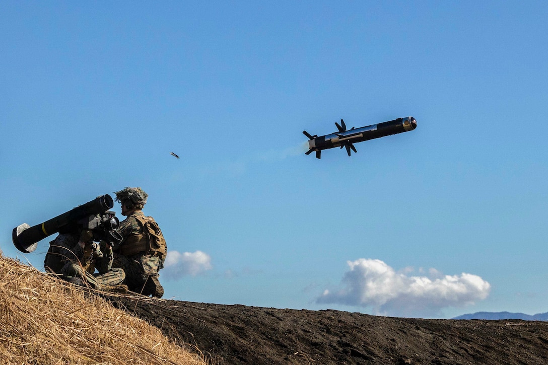 A Marine sitting on the ground fires a n over the shoulder missile while another Marine keeps watch.