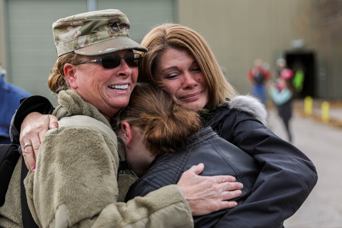 Two people embrace a uniformed service member.