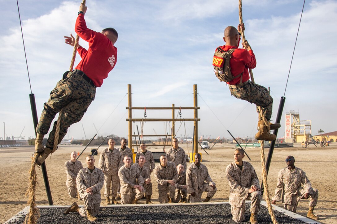 Two Marines climb ropes as other Marines watch.