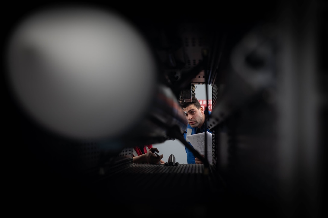 A sailor monitors insertion of a missile from the opposite end.