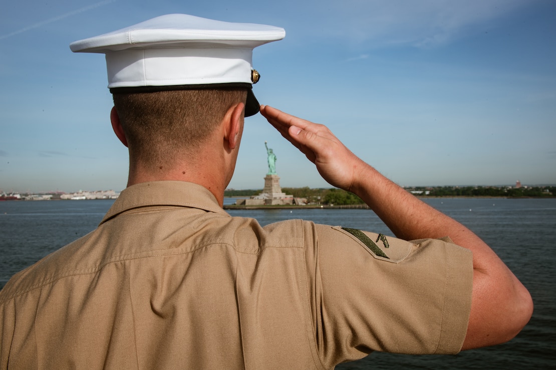 A U.S. Marine mans the rails aboard the USS Bataan with the Statue of Liberty in the distance as the ship is towed into New York Harbor in support of Fleet Week New York, 2022