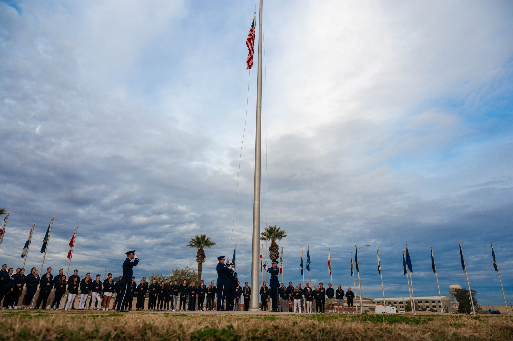 Participants of the Patriot All-American golf tournament watch as the U.S. flag is lowered during a retreat ceremony, Dec. 27, 2022, at Luke Air Force Base, Arizona.