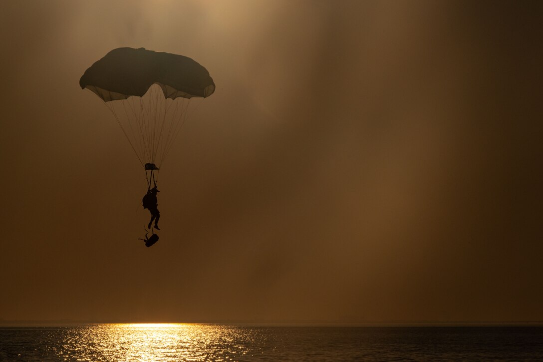 A parachutist prepares to land in the water at twilight.