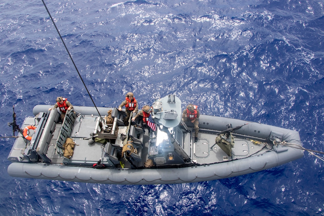 A large inflatable boat is lowered by a cable into the ocean.