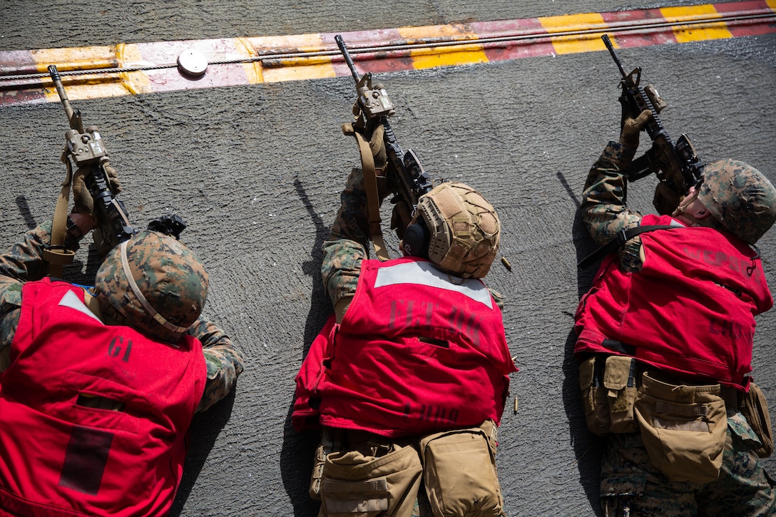 Three Marines aim rifles in the prone position on the deck of a ship.