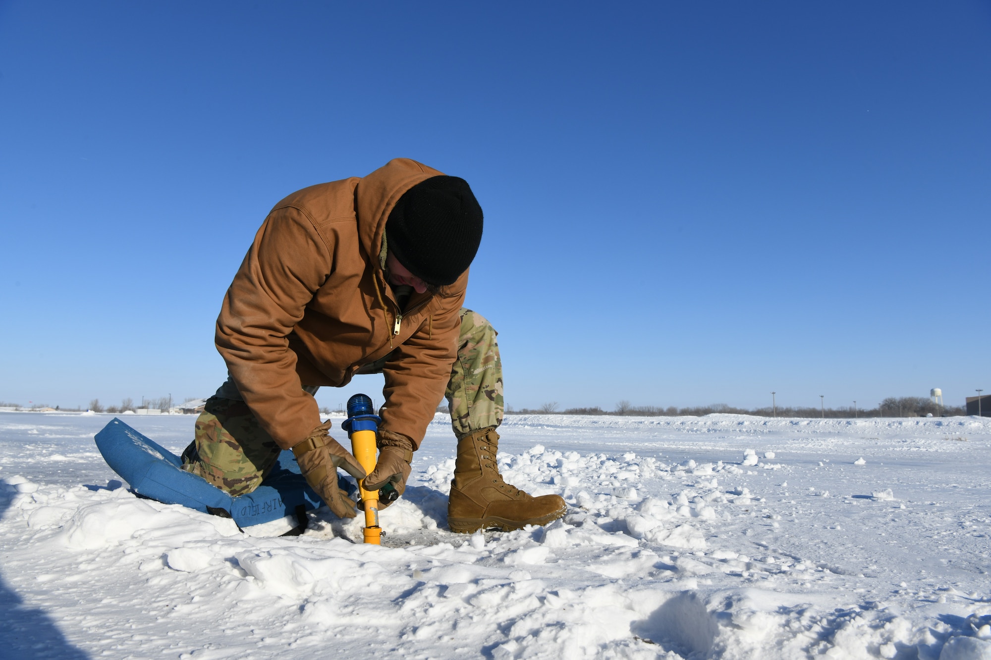 A man wearing a brown coat kneels in snow to fix a light.