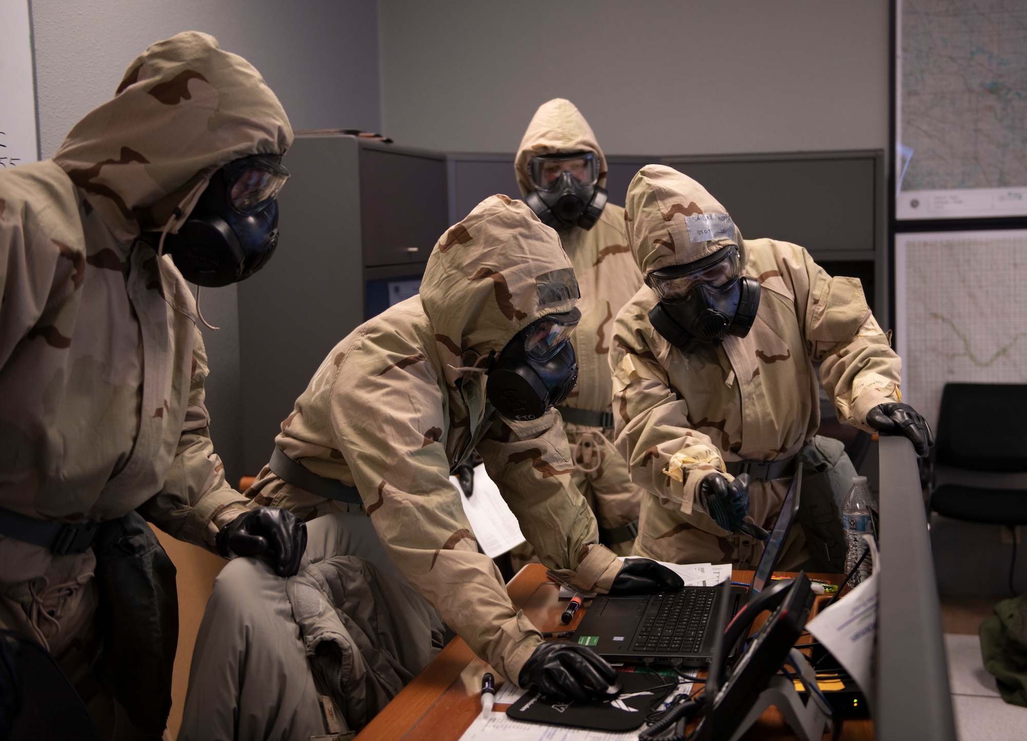 Four people in chemical gear look at a computer.