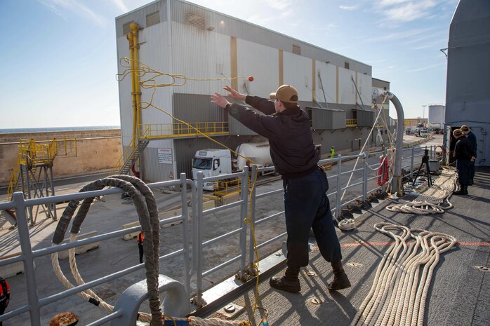 (Dec. 30, 2022) Seaman Austin Re, assigned to the Ticonderoga-class guided-missile cruiser USS Leyte Gulf (CG 55), throws a heaving ball to the pier as the ship arrives in Palma de Mallorca, Spain, for a scheduled port visit, Dec. 30, 2022. The George H.W. Bush Carrier Strike Group is on a scheduled deployment in the U.S. Naval Forces Europe area of operations, employed by U.S. Sixth Fleet to defend U.S., allied and partner interests.