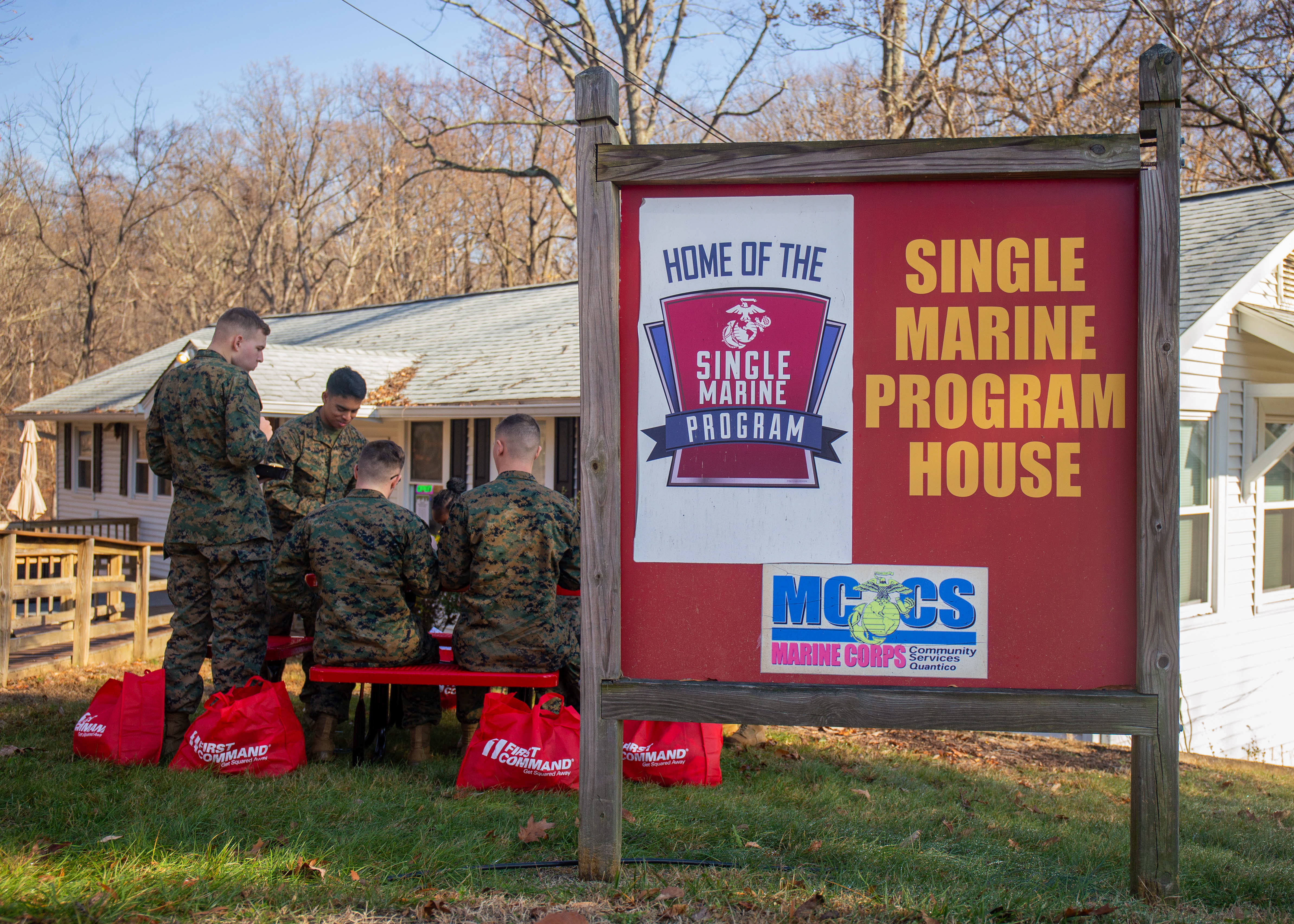 A small group of Marines sitting at a picnic table eating next to a red sign.