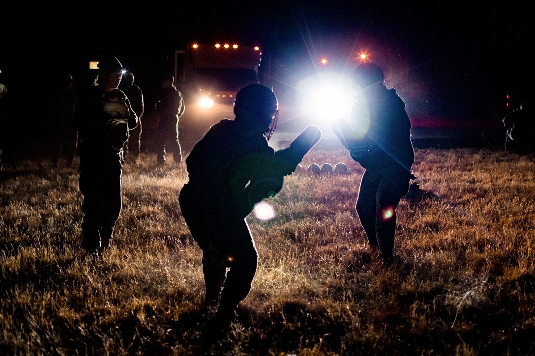 Marines participate in a martial arts event in the dark illuminated be car headlights.