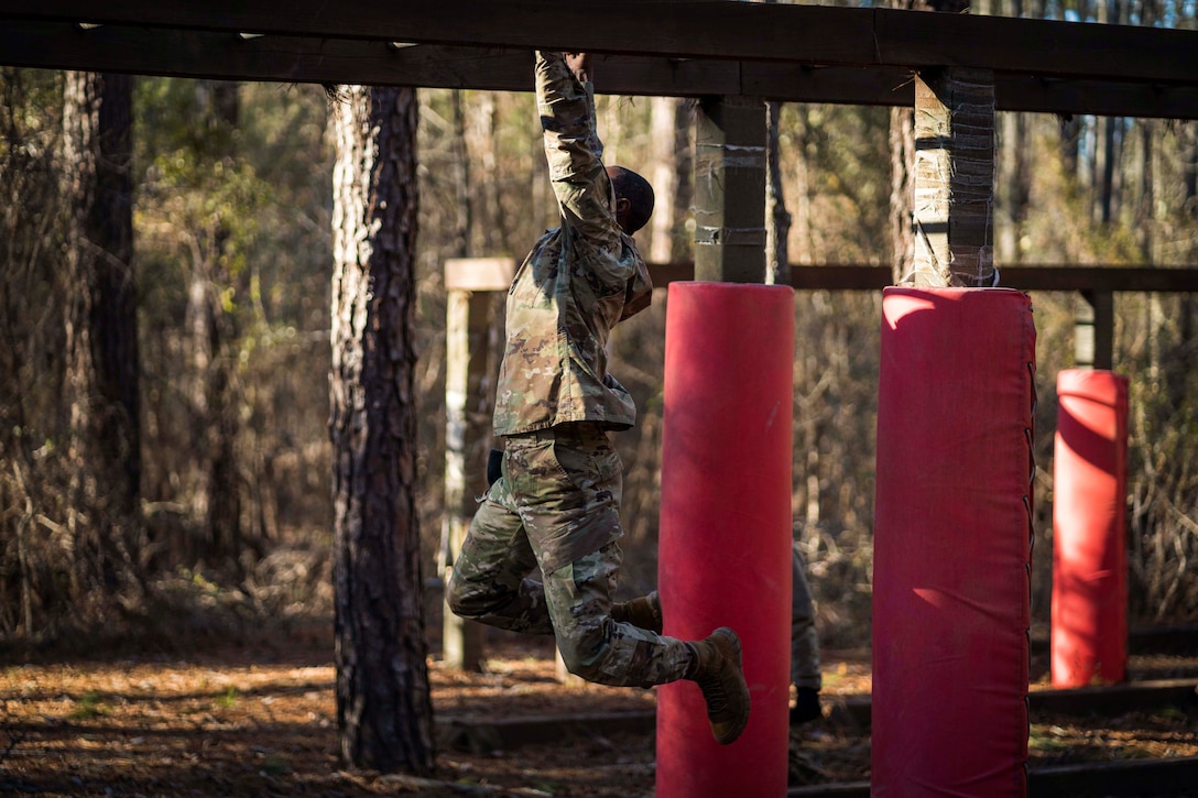 A soldier climbs across monkey bars in the woods.