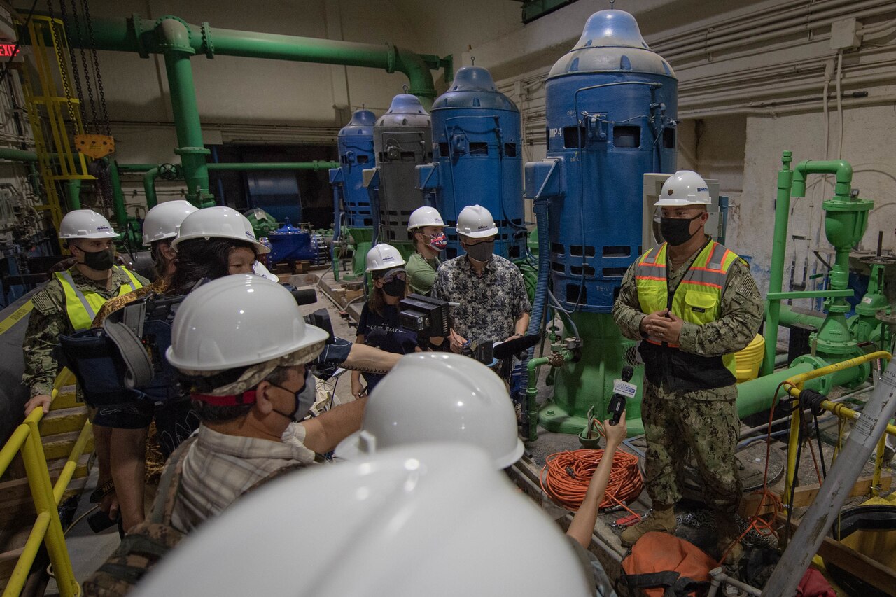 Military personnel and civilians meet in an indoors industrial area.