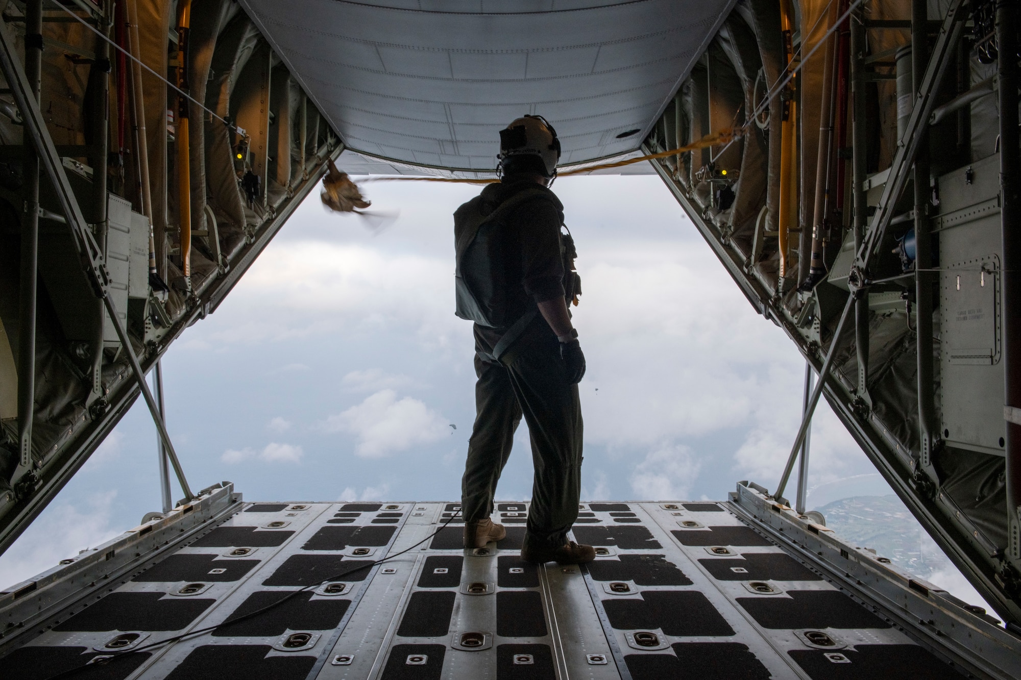 A loadmaster stands at the end of the tail of the aircraft, looking out over the horizon