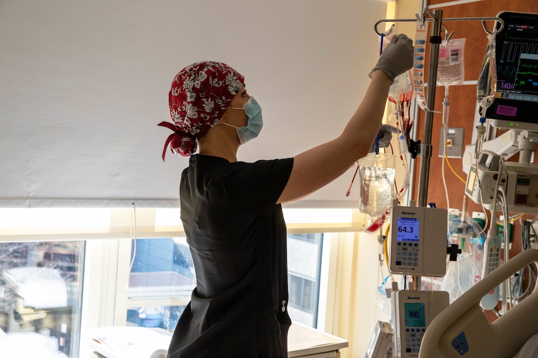 A soldier wearing a face mask and gloves removes a blood bag during COVID-19 response operations.