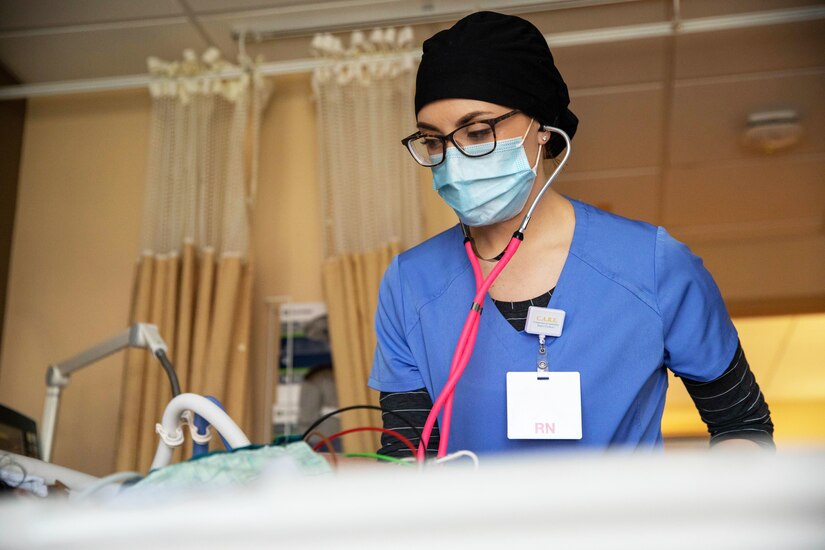 A soldier wearing a face mask monitors a patient’s breathing during COVID-19 response operations.