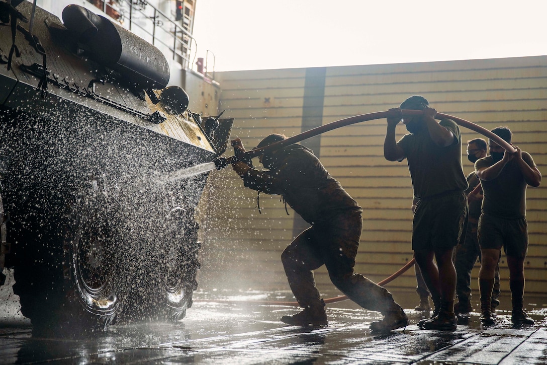 Marines use a fire hose to wash a vehicle aboard a ship at sea.