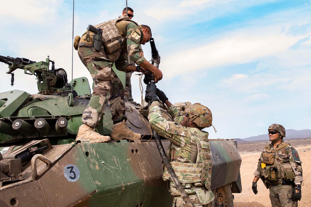 U.S. and French troops work on an armored vehicle in the desert.