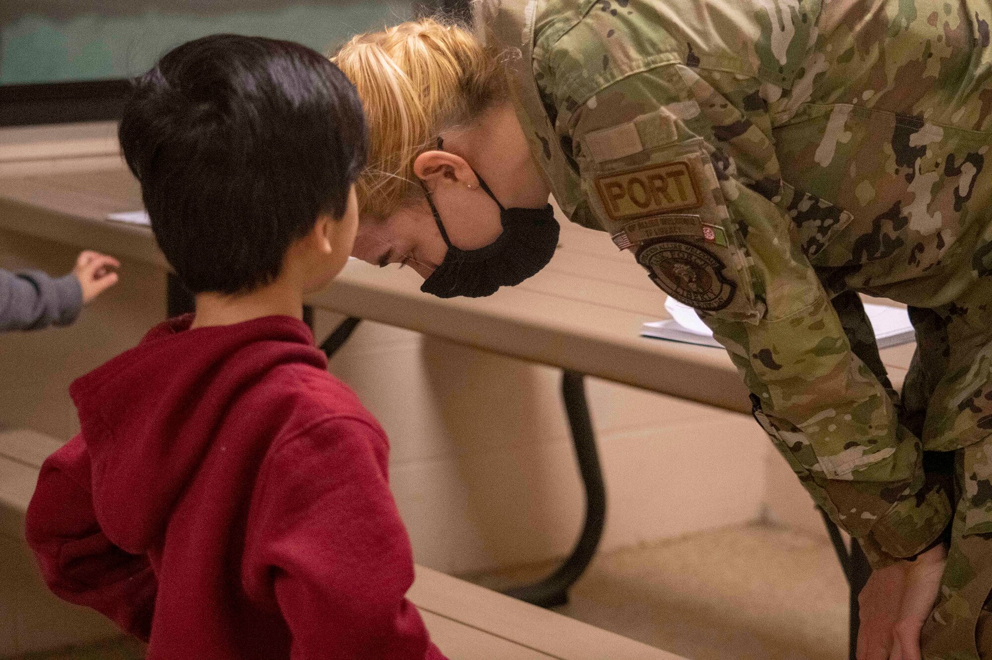 Airman 1st Class Scotie Wood, 87th Aerial Port Squadron cargo-processing apprentice currently assigned to the Task Force-Liberty Joint Readiness Center floor operations, listens to a question from an Afghan child while teaching English in Liberty Village on Joint Base McGuire-Dix-Lakehurst, New Jersey, Feb. 1, 2022. The Department of Defense, through U.S. Northern Command, and in support of the Department of Homeland Security, is providing transportation, temporary housing, medical screening, and general support for at least 11,000 Afghan evacuees at Liberty Village, in permanent or temporary structures, as quickly as possible. This initiative provides Afghan personnel essential support at secure locations outside Afghanistan.