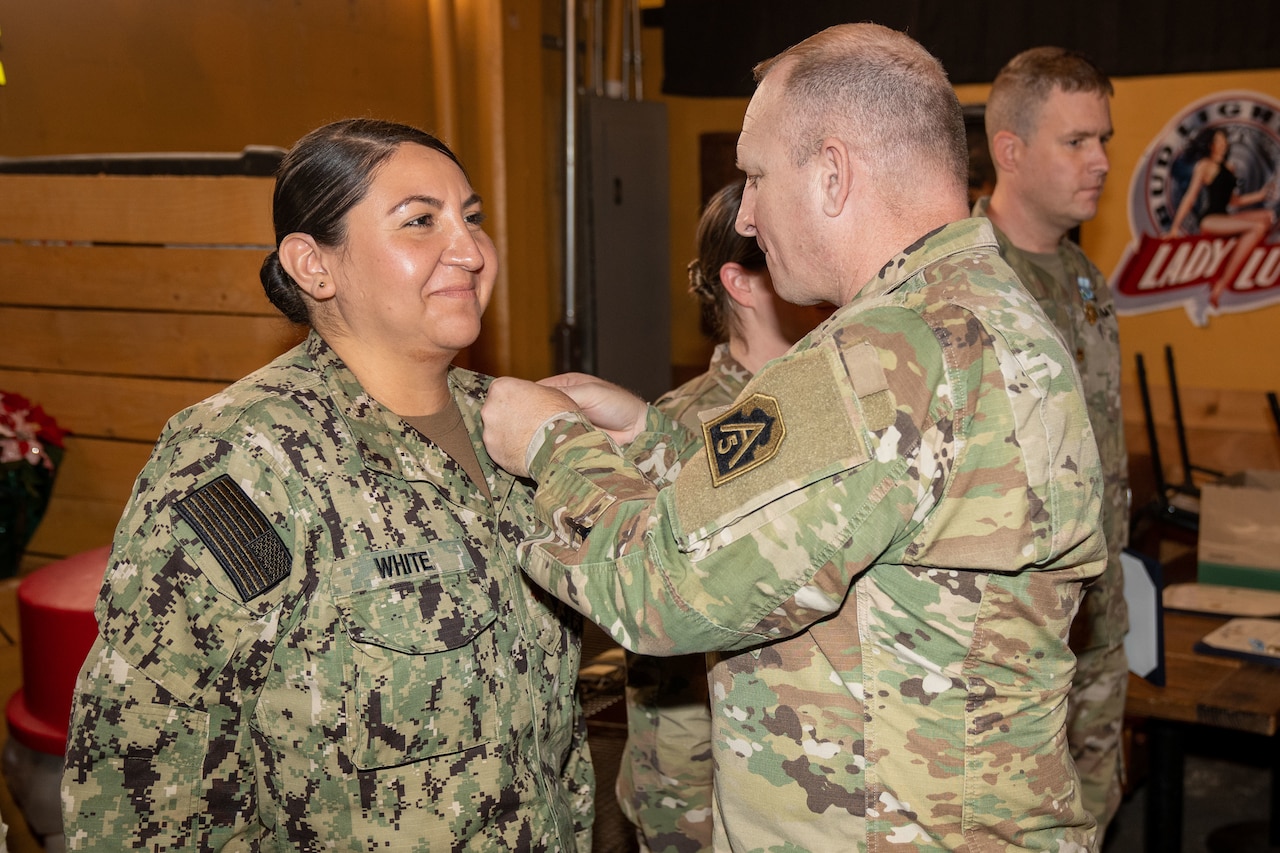 A man in military uniform pins an award on a woman in military uniform.