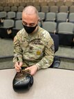 An Army soldier signing a glove with a pen.