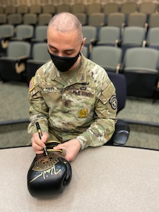 An Army soldier signing a glove with a pen.