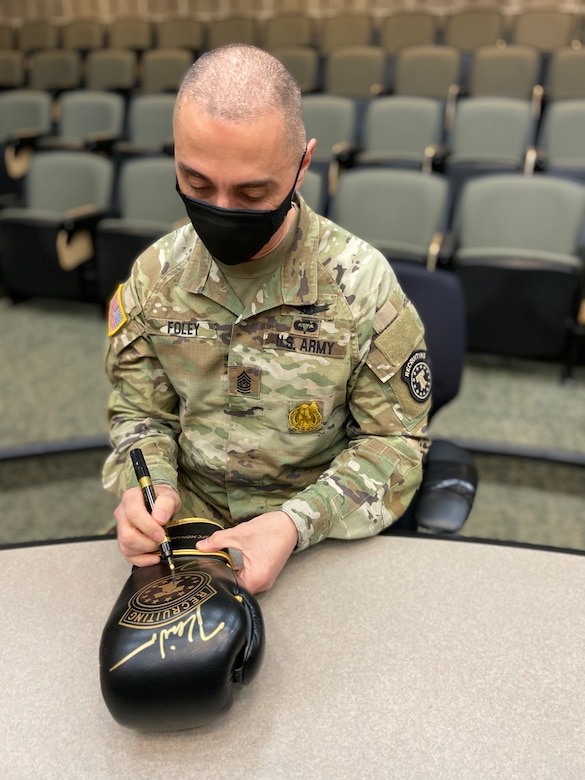 An Army soldier signing a glove with a pen.